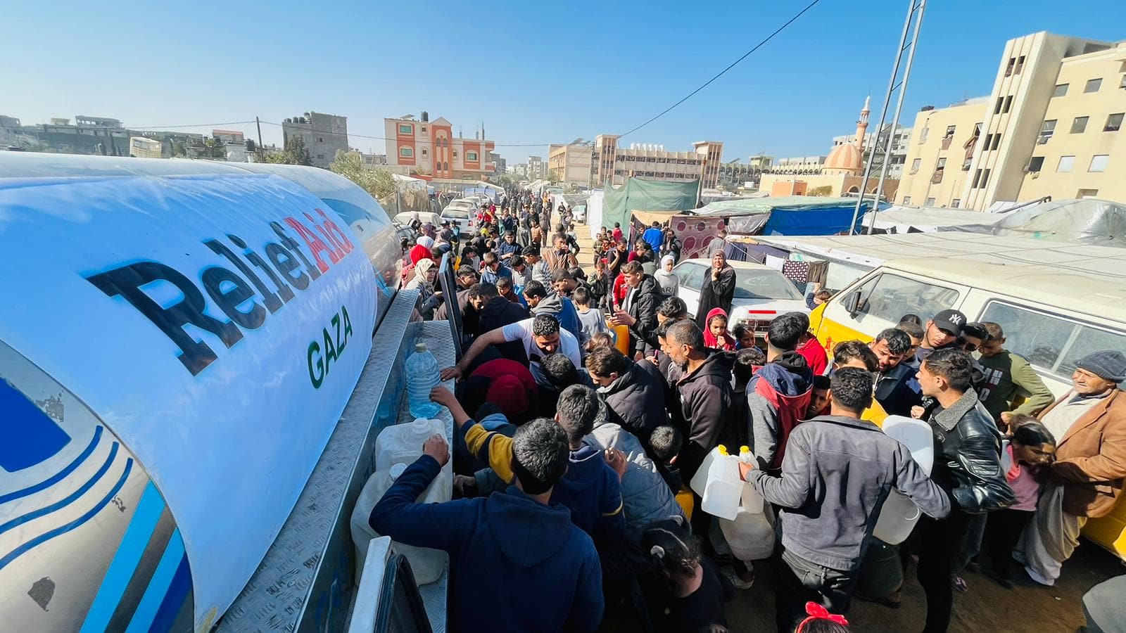 A large group of people collecting water from a ReliefAid water truck.